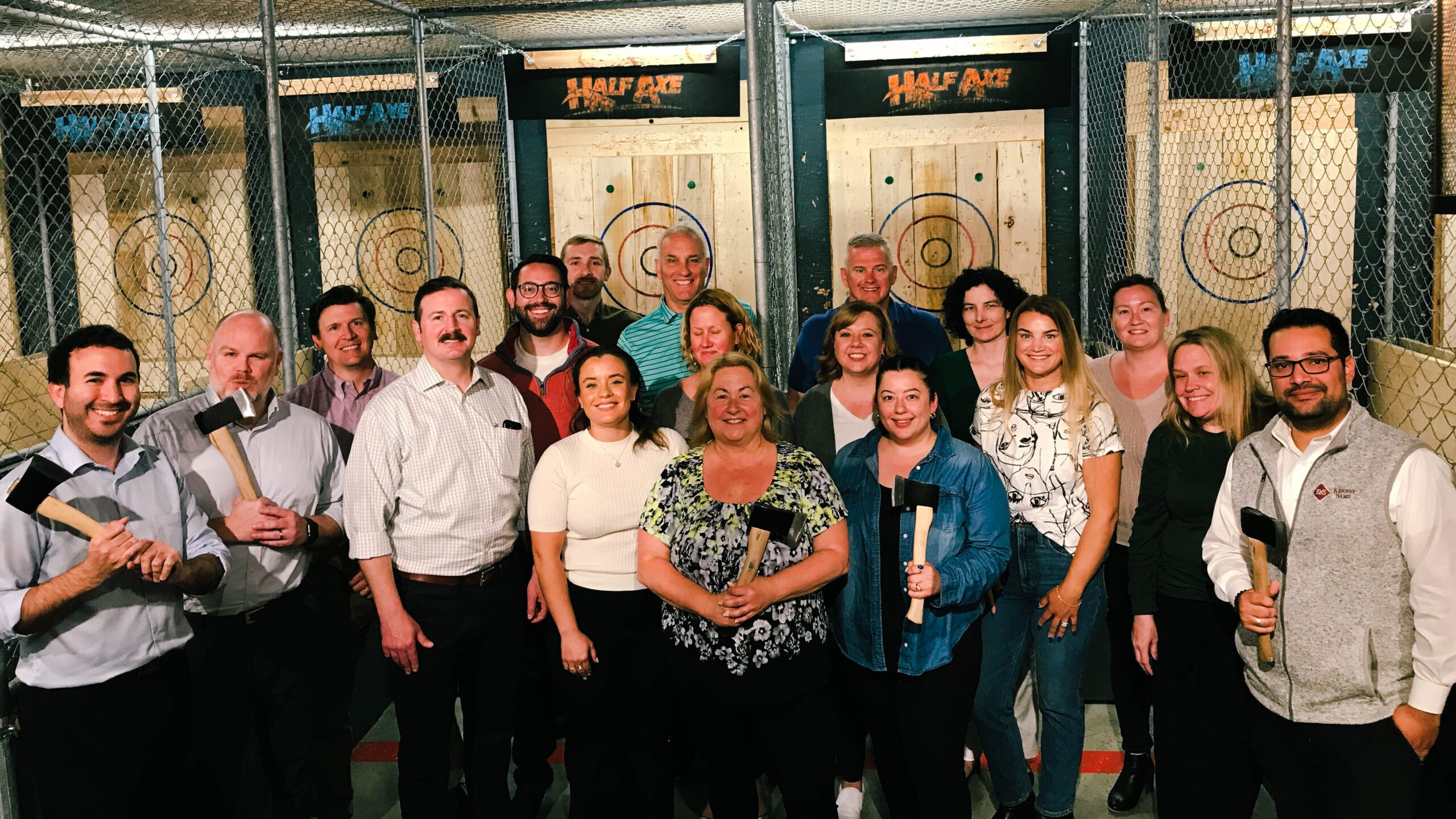 a group of people who made a booking posing for a picture and smiling in a half axe throwing bay at a group outing